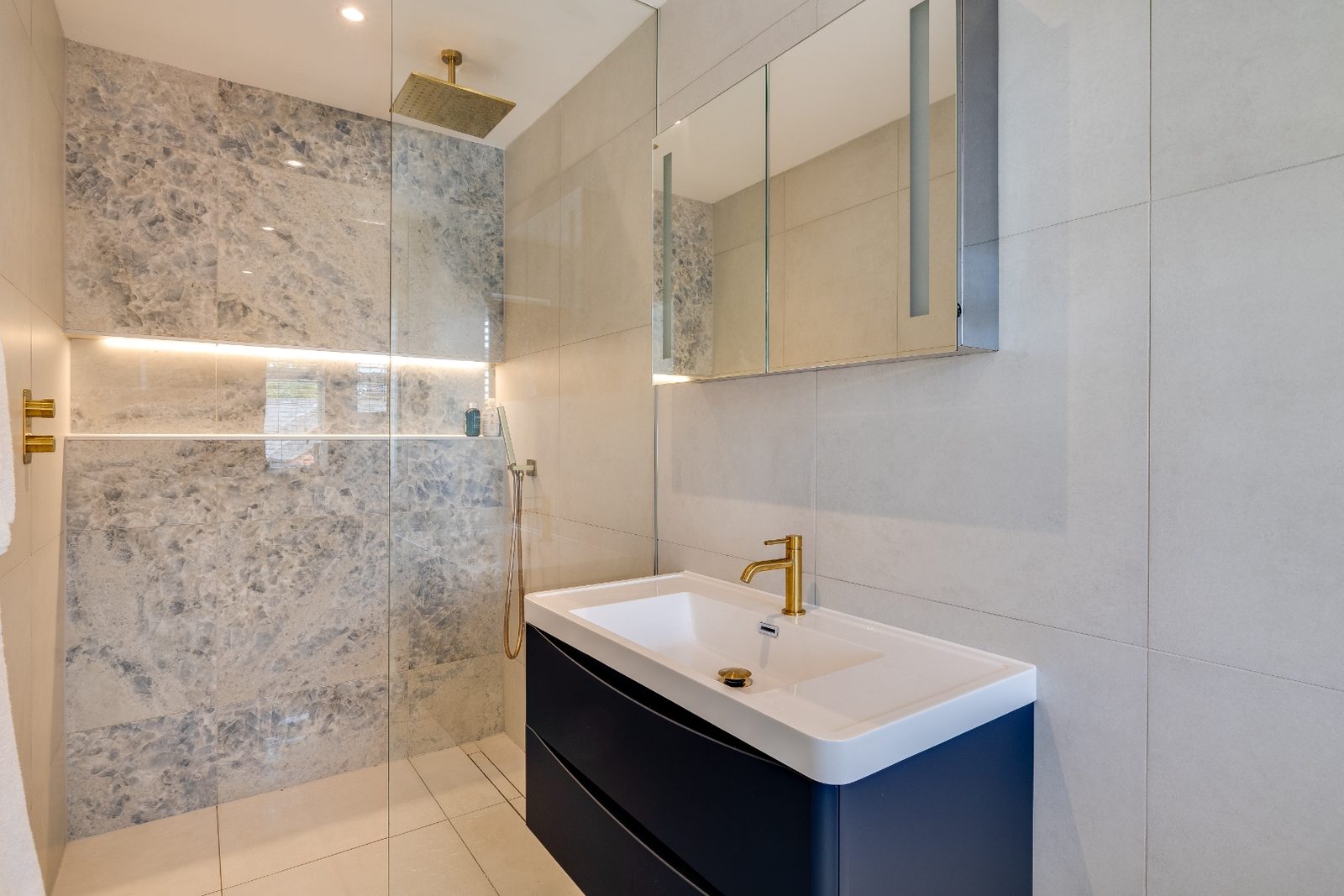 Renovated en-suite bathroom with marble tiling, brass rain shower and navy vanity unit