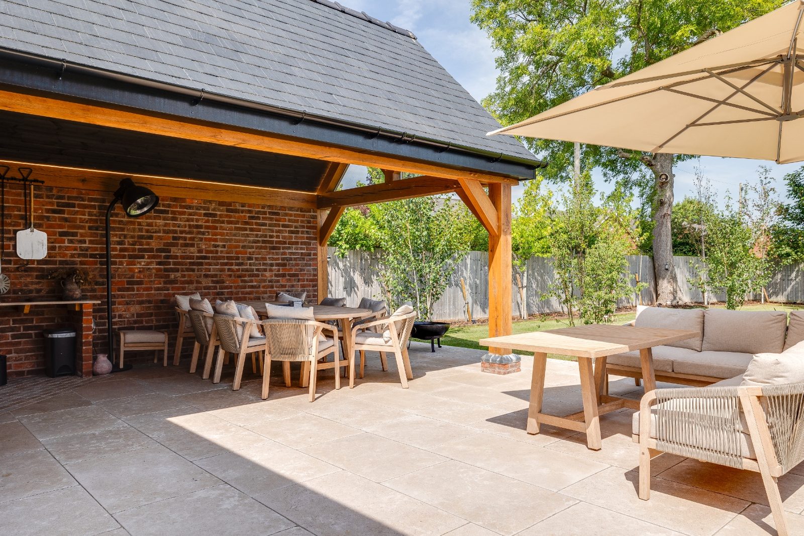 Covered oakframe outdoor dining and lounge area with stone paving and garden view
