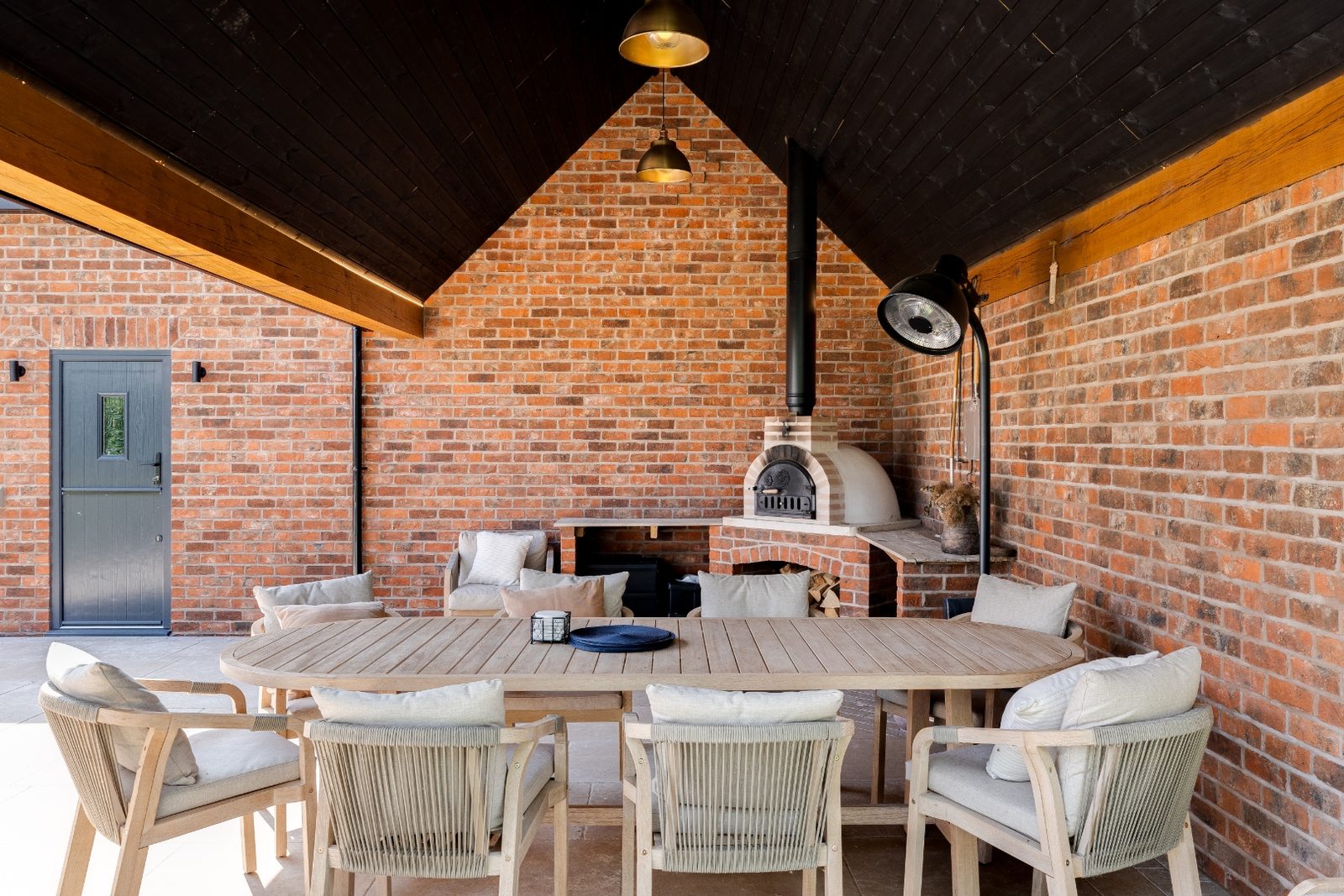 Oakframe pavilion interior with exposed brick, wood-fired pizza oven and dining table