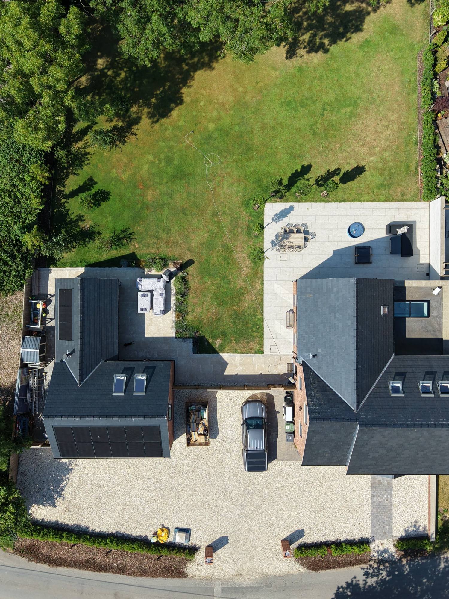 Top-down aerial of a completed Built Clear home with slate roof, solar panels, garden and paved terrace.